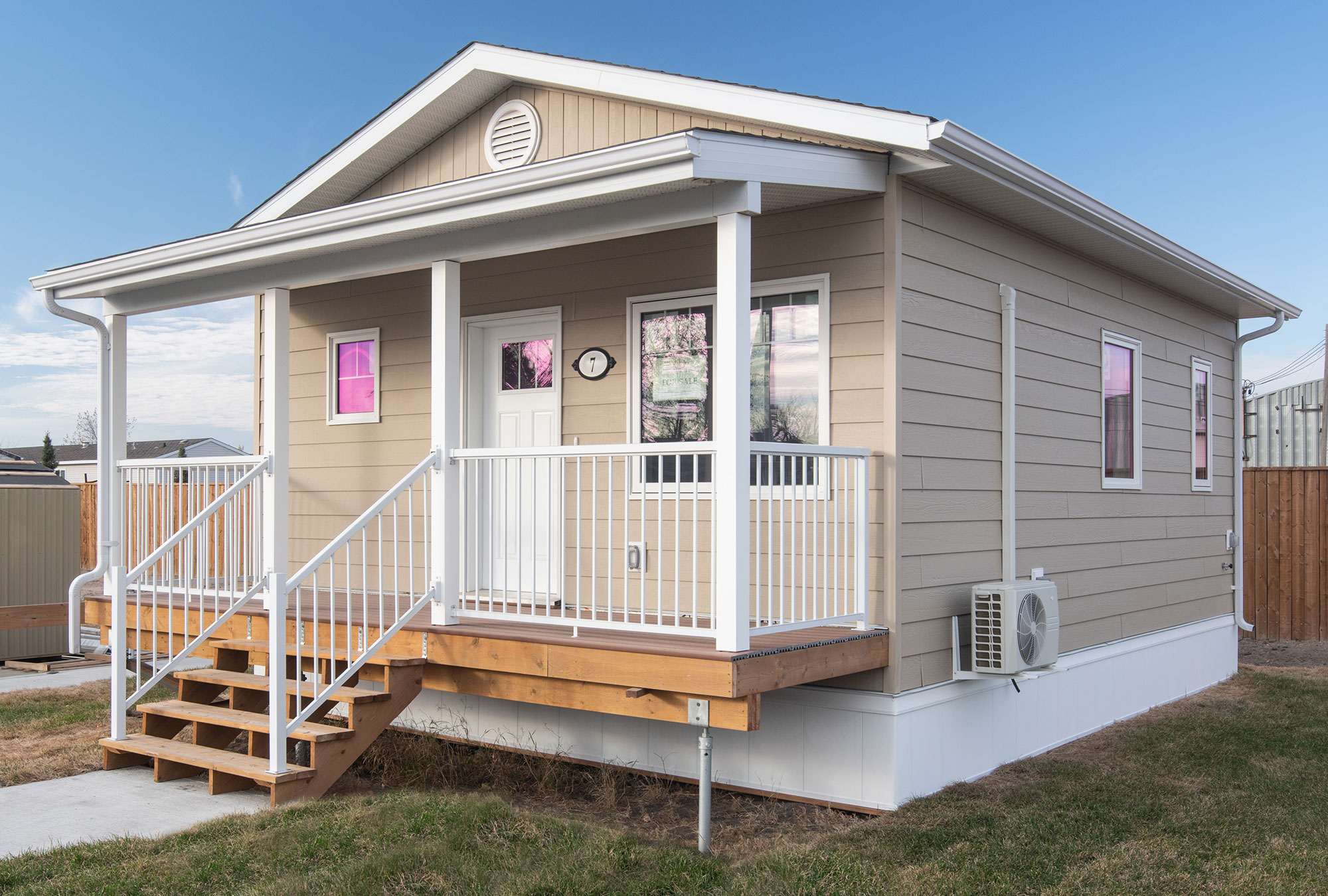 Exterior view of the front of the Prairie Crocus home style at Glendale Homes Park in Brandon, Manitoba. The home has front porch with white metal railing. The home has beige siding and white trim.